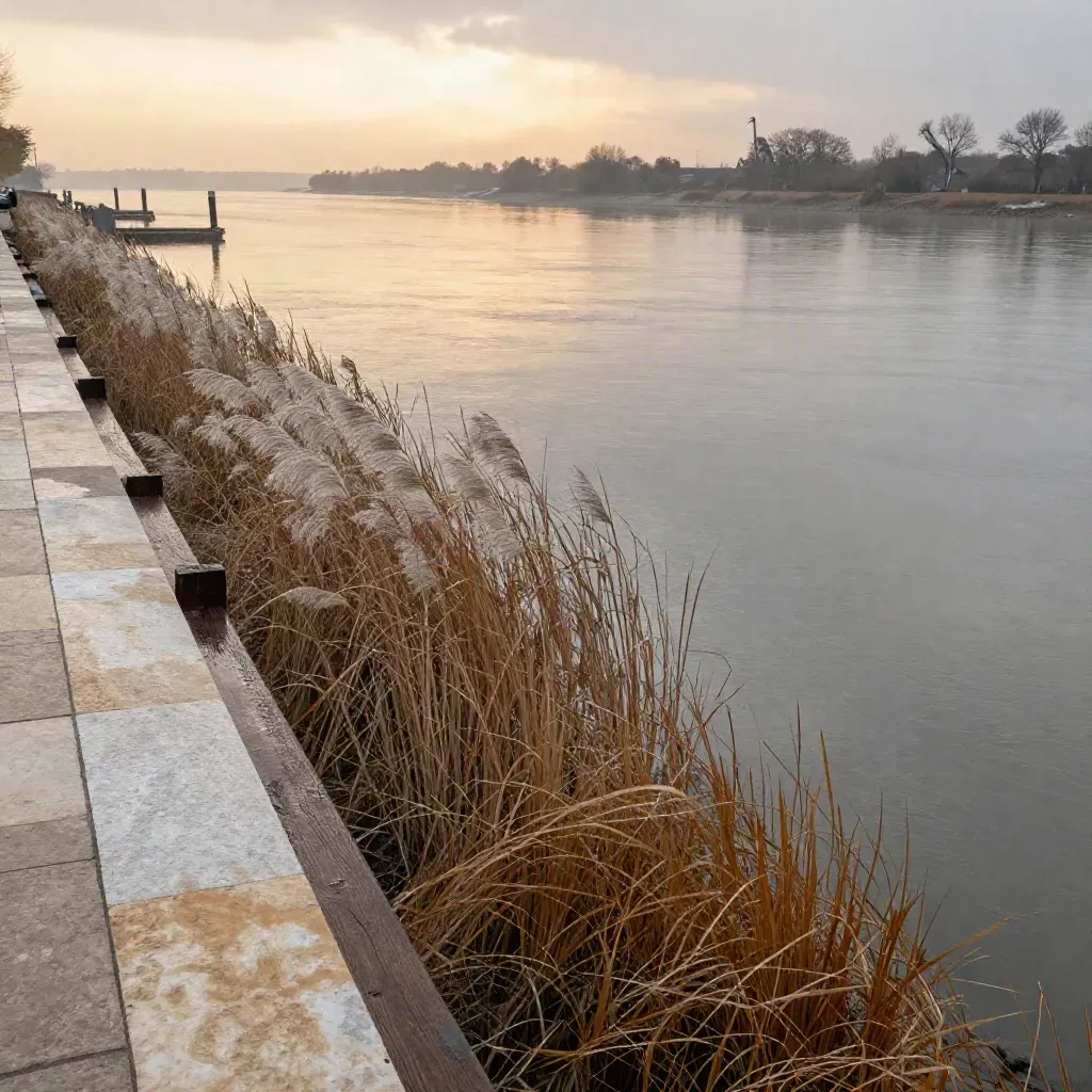 Tidal river dock at dusk with reeds, haze, stone edges and blurred cranes.